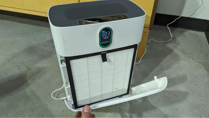 A hand opens up the front grill on the Morento Air purifier, showing the HEPA filter within.