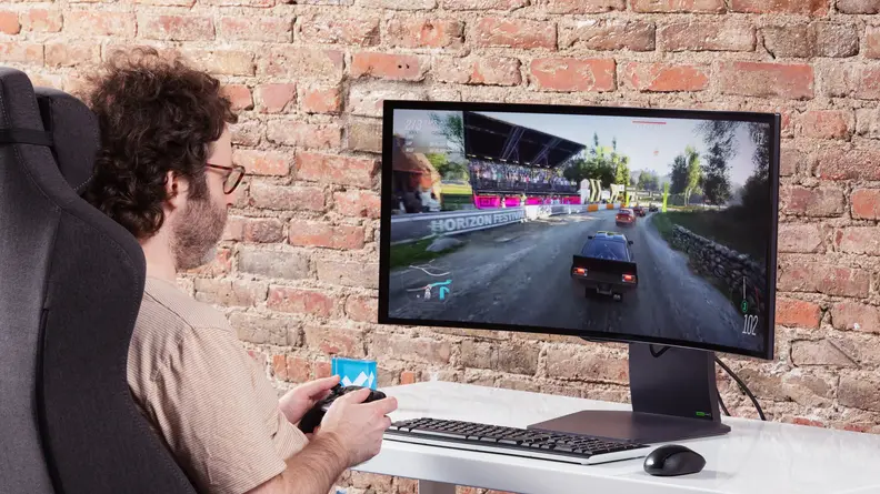 A man sitting in front of the LG UltraGear OLED 34GS95QE-B playing a game