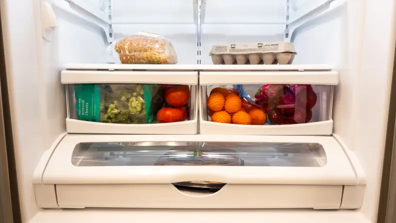 A refrigerator is stocked with groceries: bread, eggs, broccoli, tomatoes, apples, and oranges.
