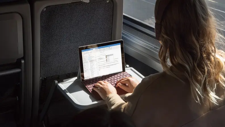 A person in a train using a Windows Surface with Windows S Mode enabled.