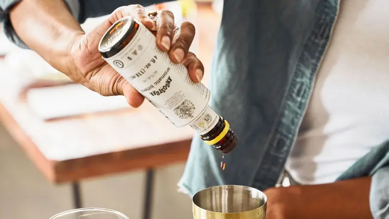 Close-up: An individual pours aromatic bitters into a cocktail shaker.