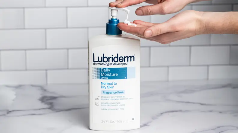 A person's hand pumping a white bottle of body lotion.