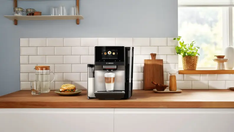 Bosch espresso machine with a prepared latte at the base, shot in a kitchen setting