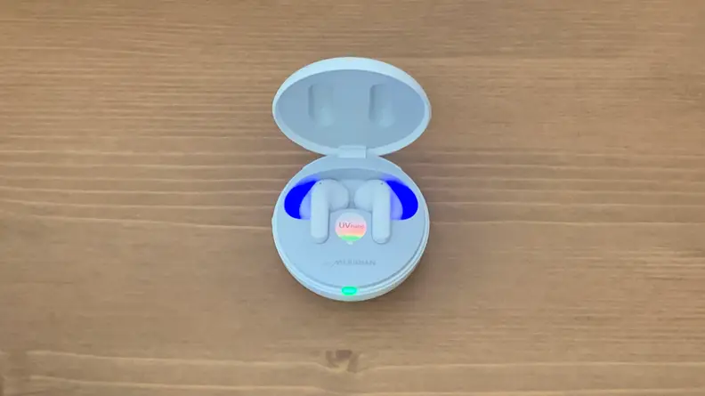 The interior of the open LG T90Q earbuds case glows blue as it sits on a wooden table.