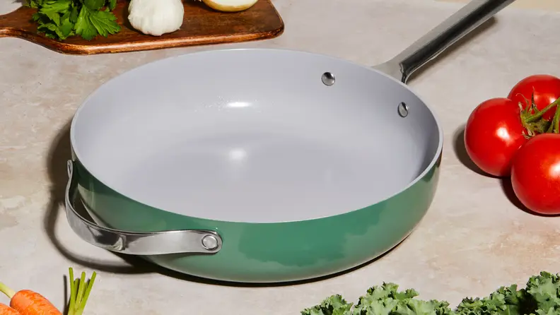 A green Caraway frying pan on a kitchen counter surrounded by fresh vegetables, included as a free gift with the HelloFresh promo code.