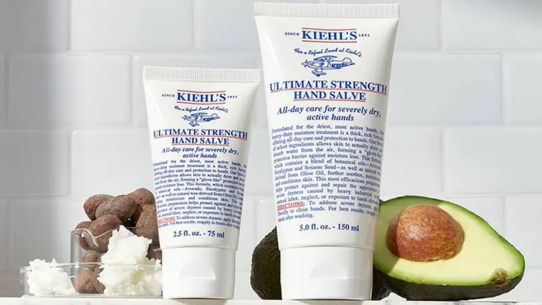 2 sizes of Kiehl’s Ultimate Strength Hand Salve on counter next to avocado