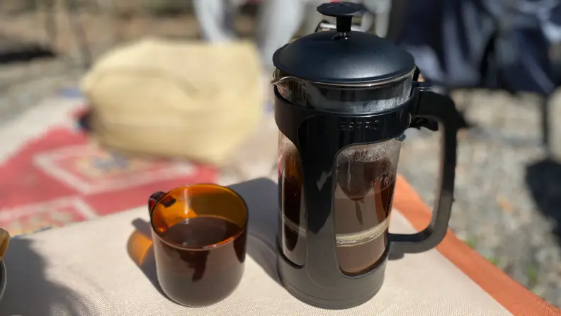 An Espro P3 French press with black plastic holder is pictured next to a brown-tainted glass mug on a table.