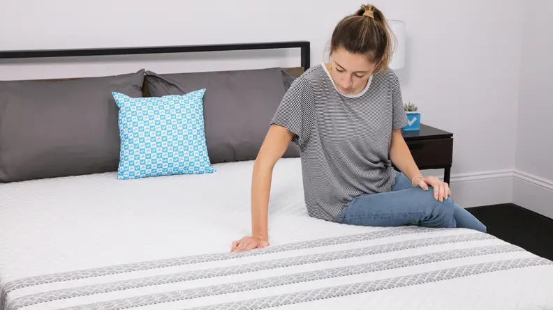 A person sitting on the Leesa Sapira hybrid mattress. They are feeling the texture of the cover with their hand.