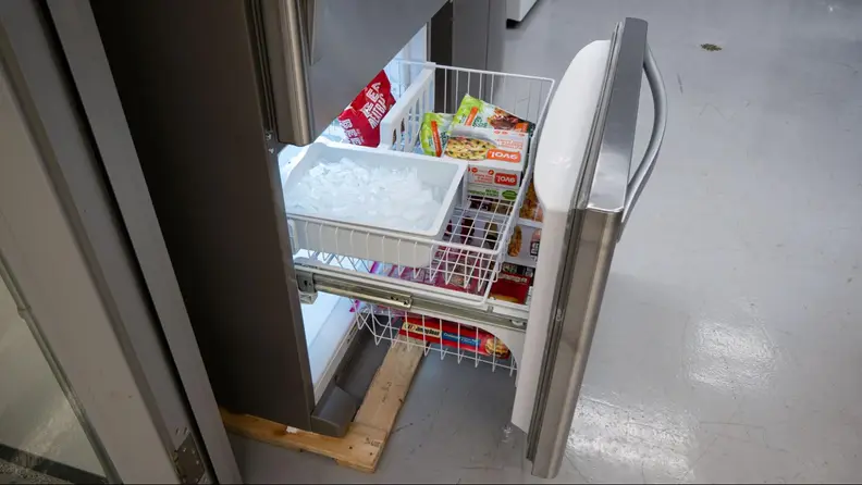 The bottom freezer drawer open with frozen food and an ice tray inside.