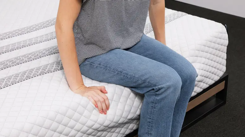 A person sitting on the edge of the Leesa Sapira hybrid mattress