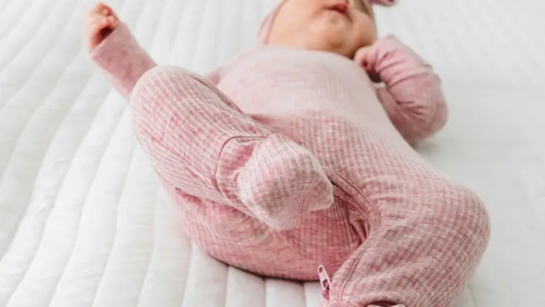 Close-up of a baby in pink footed pajamas lying on a white quilted bed.