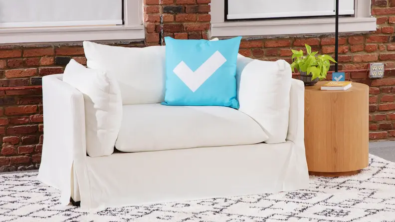 A front facing view of a white lounge chair and a circular wooden side table against a brick background.