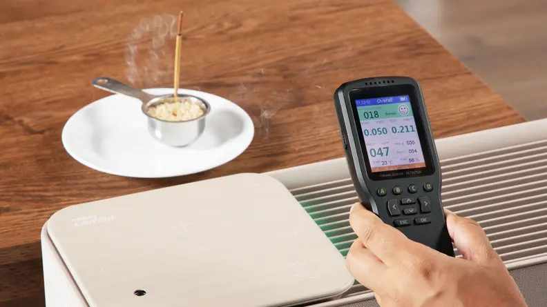 A person holding a phone with an air purifier on the ground, seemingly controlling it.
