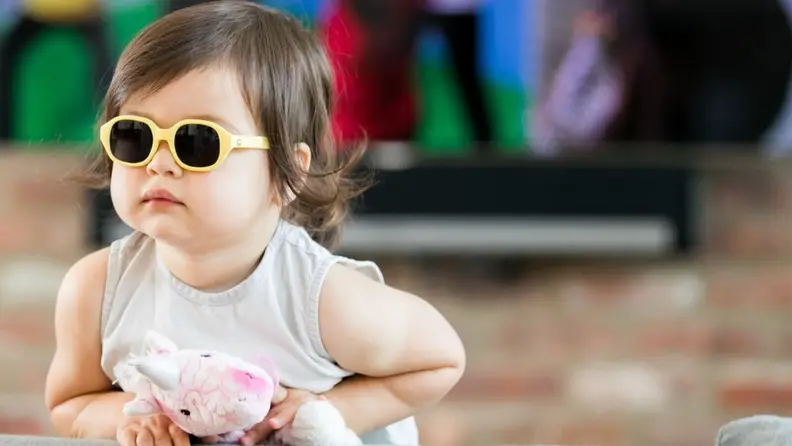 A young child wears yellow sunglasses