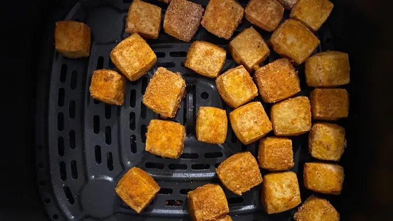 Cubes of air fried tofu sitting in the bottom of an air fryer.
