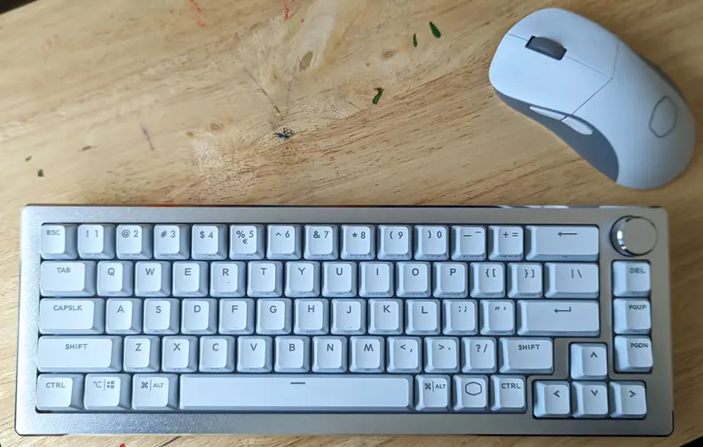 A white keyboard with a white mouse on top of a light brown desk
