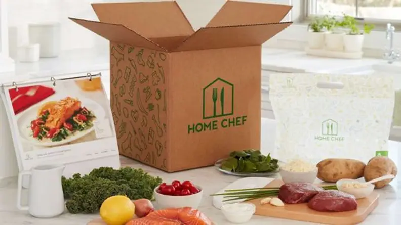 A Home Chef box on a kitchen island, with food displayed around the box.