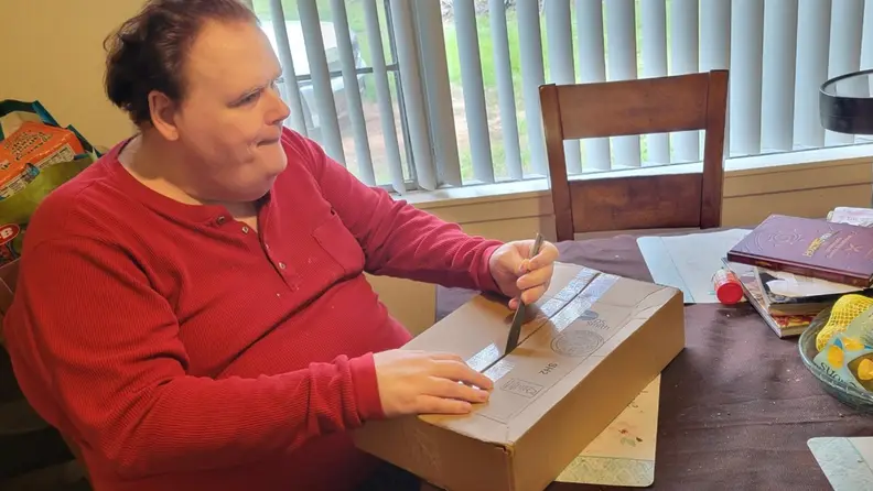 A man opening the cardboard Lego Braille Brick box with a knife.