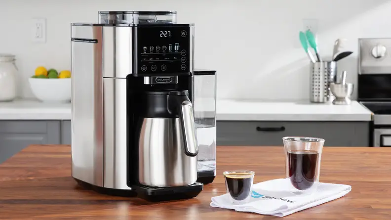 The De'Longhi TrueBrew on a counter, next to two different size coffee cups.