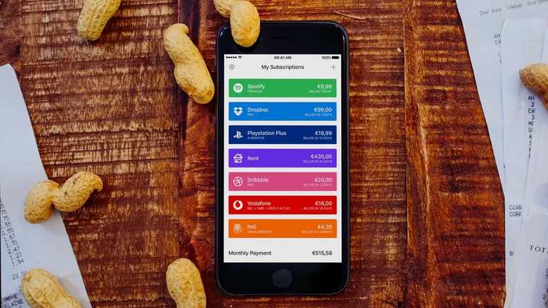An iPhone resting on a bed of wood with peanuts scattered about, with an iPhone in the center showing Bobby's home screen with a list of subscriptions.