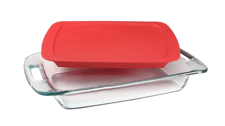 An image of a glass Pyrex baking dish with a red lid sat slightly askew on top of it, on a white background.