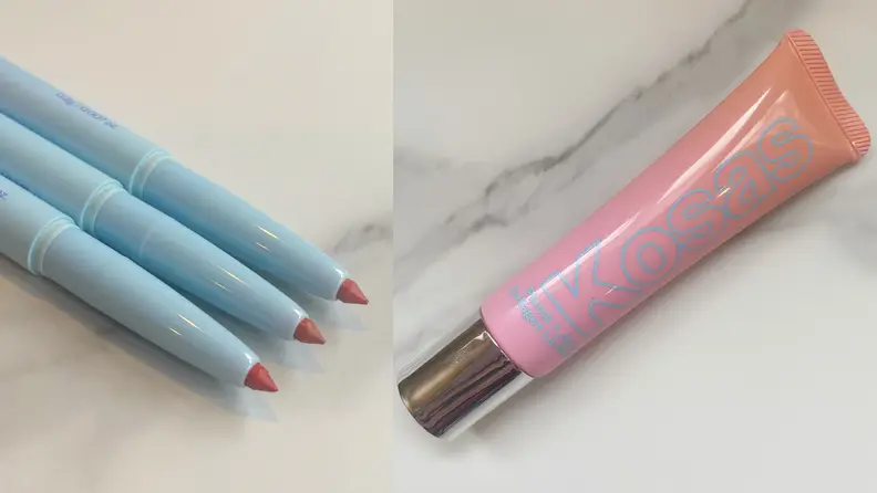 On the left: Three lip liners in different shades lay next to each other on a marble tabletop. On the right: A pink tube of lip gloss lays on a marble countertop.