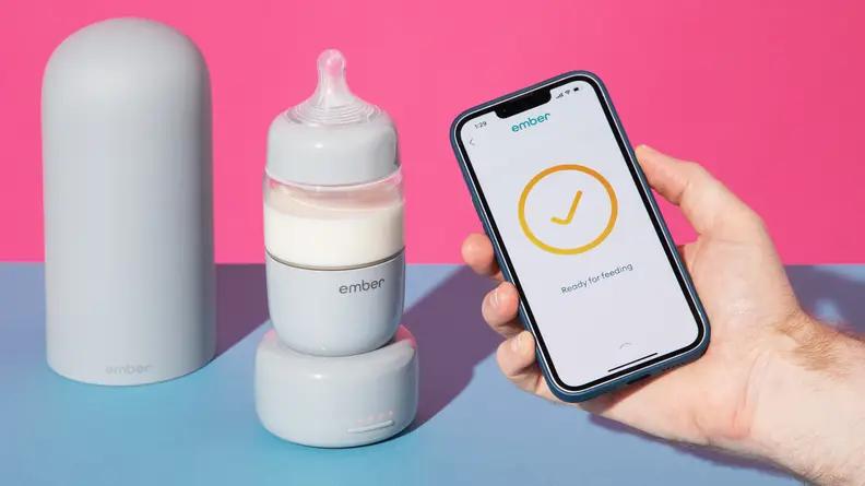 A person holding a smart phone next to the Ember Baby Bottle System on a blue and pink background.
