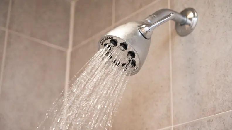 A Speakerman shower head shown spraying water in a tiled shower stall.