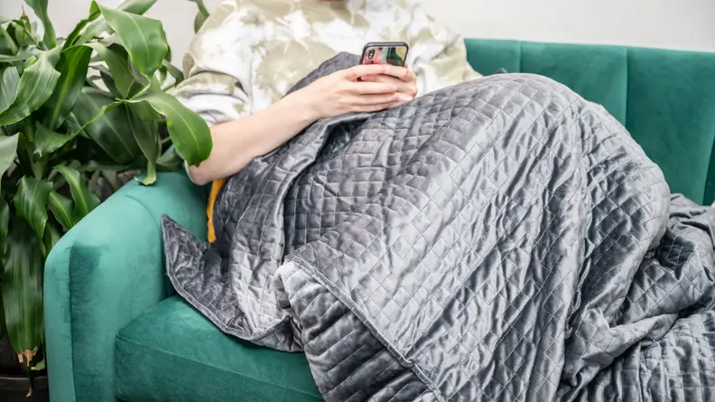 Person sitting on couch wearing blanket while looking at smartphone smartphone.