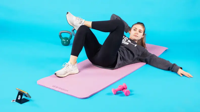 Person laying on yoga mat with one arm behind their head and their other arm outstretched while completing a workout.