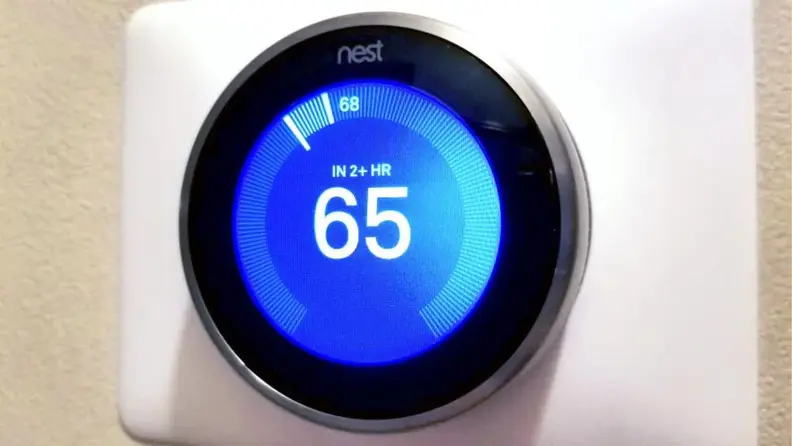 A Nest smart thermostat on a white wall.