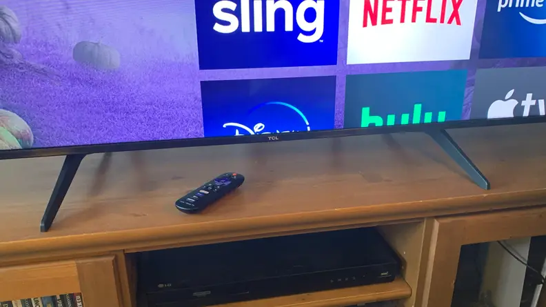 A closeup of the TCL 5-Series feet with a Roku remote sitting on a wooden table.