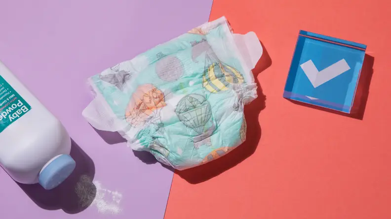 A single Honest diaper in the middle of a bottle of talcum powder and a blue paperweight.