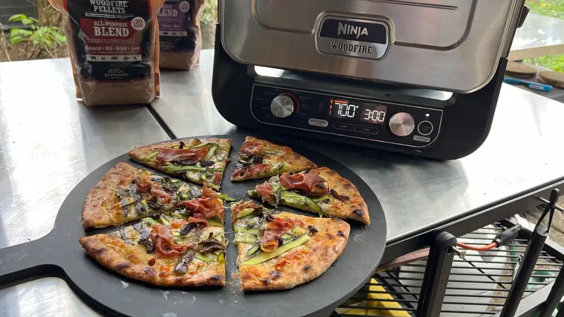 Sliced pizza pie in front of the Ninja Woodfire Outdoor Oven.