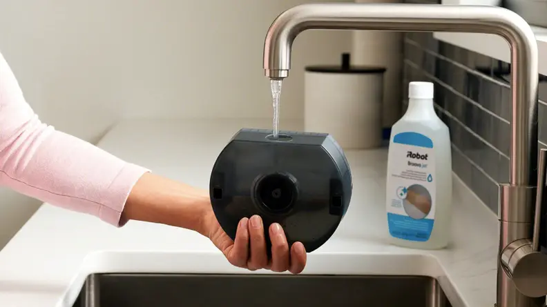 Someone pours water into a robot mop with a bottle of cleaning fluid on the counter
