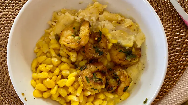 A bowl of  grilled shrimp with creamy grits and corn is in the middle of the image.
