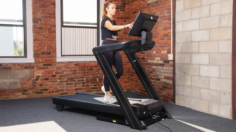 A woman picking a workout class on the NordicTrack Commercial 1750's HD touchscreen.