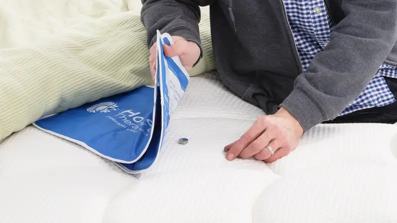 A person placing a heat sensor under a heating pad on the surface of the DreamCloud mattress.