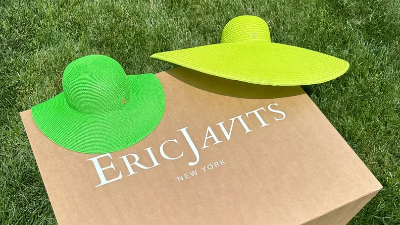 A green and neon green hat lay on top of an Eric Javits cardboard box.