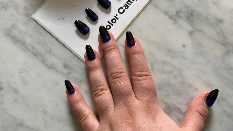 A hand wearing press-on nails laying on a marble tabletop in front of a set of matching press-ons.