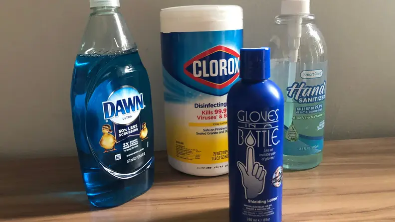 Assorted cleaning products and moisturizer sitting on wooden surface