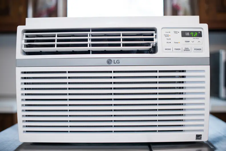 A white LG LW8016ER Window AC unit is placed on a table in front of a window, in contention for a top slot among the best window air conditioners..