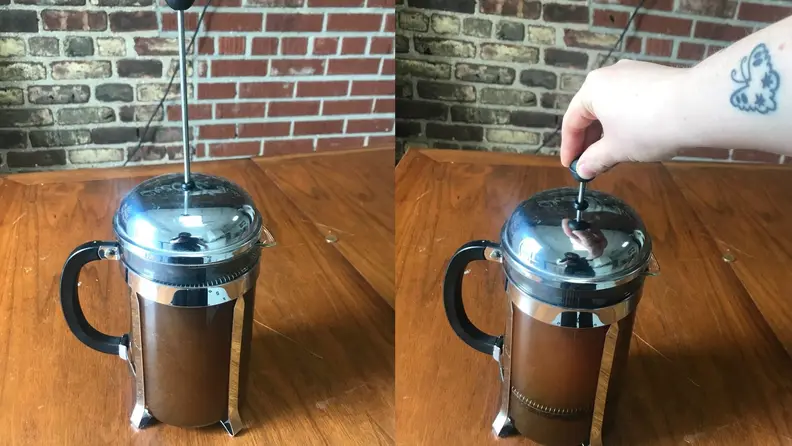 A person pushes the plunger on a French press coffee maker to make cold brew coffee.