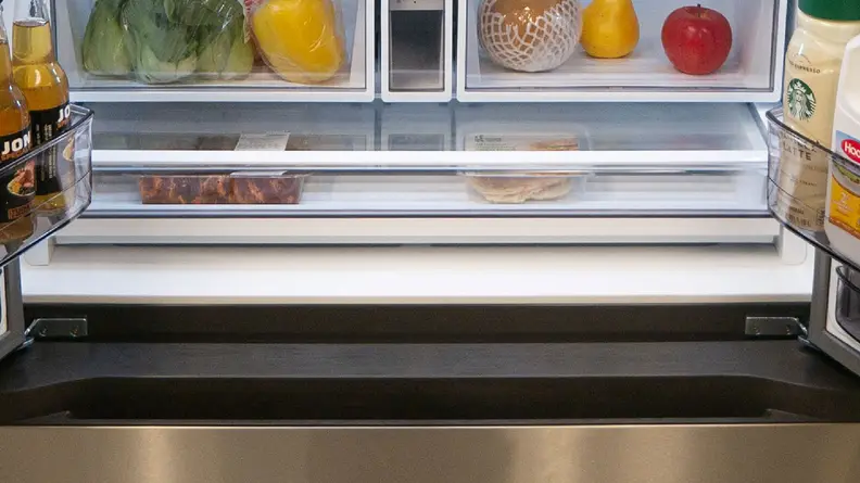 A close-up of the deli drawer at the bottom of the fridge compartment, stocked with food.