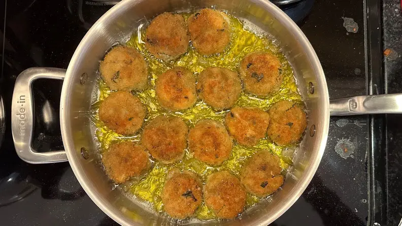Eggplant meatlballs frying in a stainless steel sauté pan.