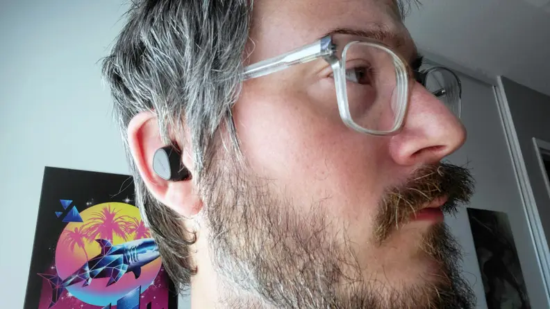 Jabra's all-black, matte earbuds sit in a man's ear beneath glasses and a short mop of salt and pepper hair.