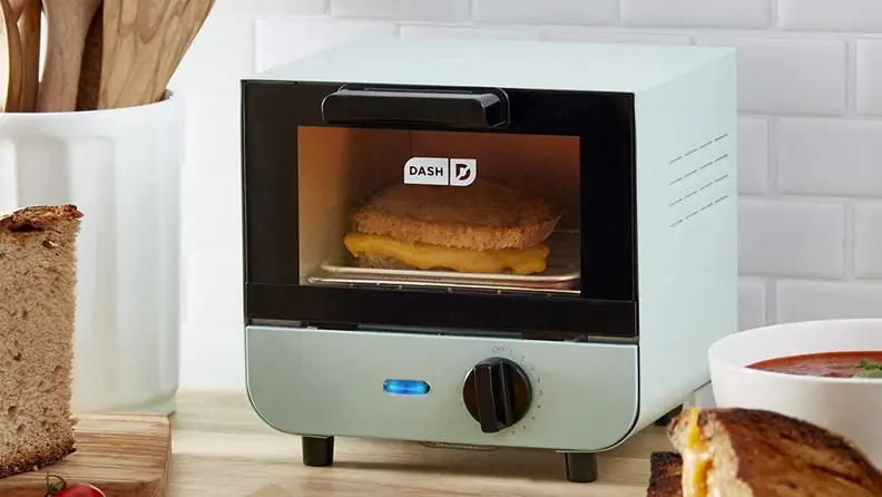 A light blue mini toaster oven sits on a kitchen countertop with a cooked grilled cheese inside.