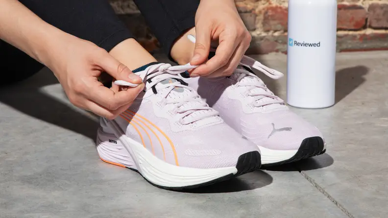 A person ties the laces on a pair of white running shoes outside.