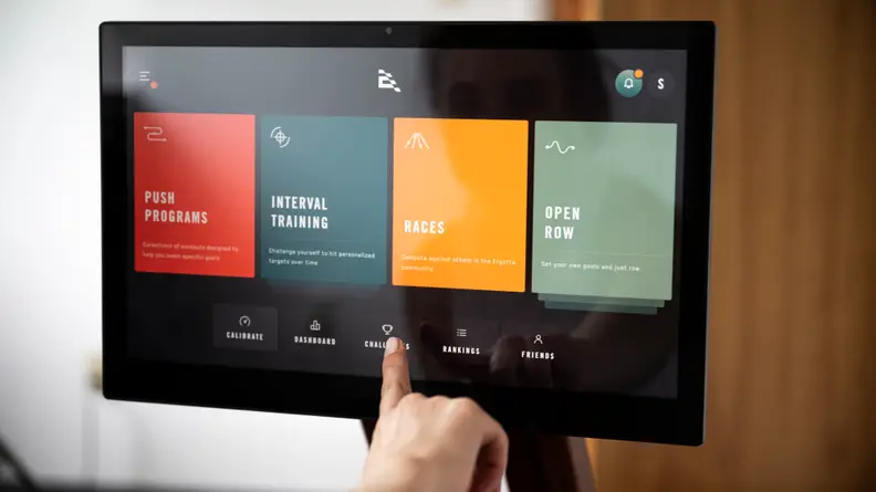 Hand pointing at Ergatta homescreen showing push programs, intervals, races, open row.