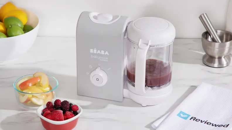 A Beaba Babycook Express sitting on a kitchen counter next to a bowl of berries.